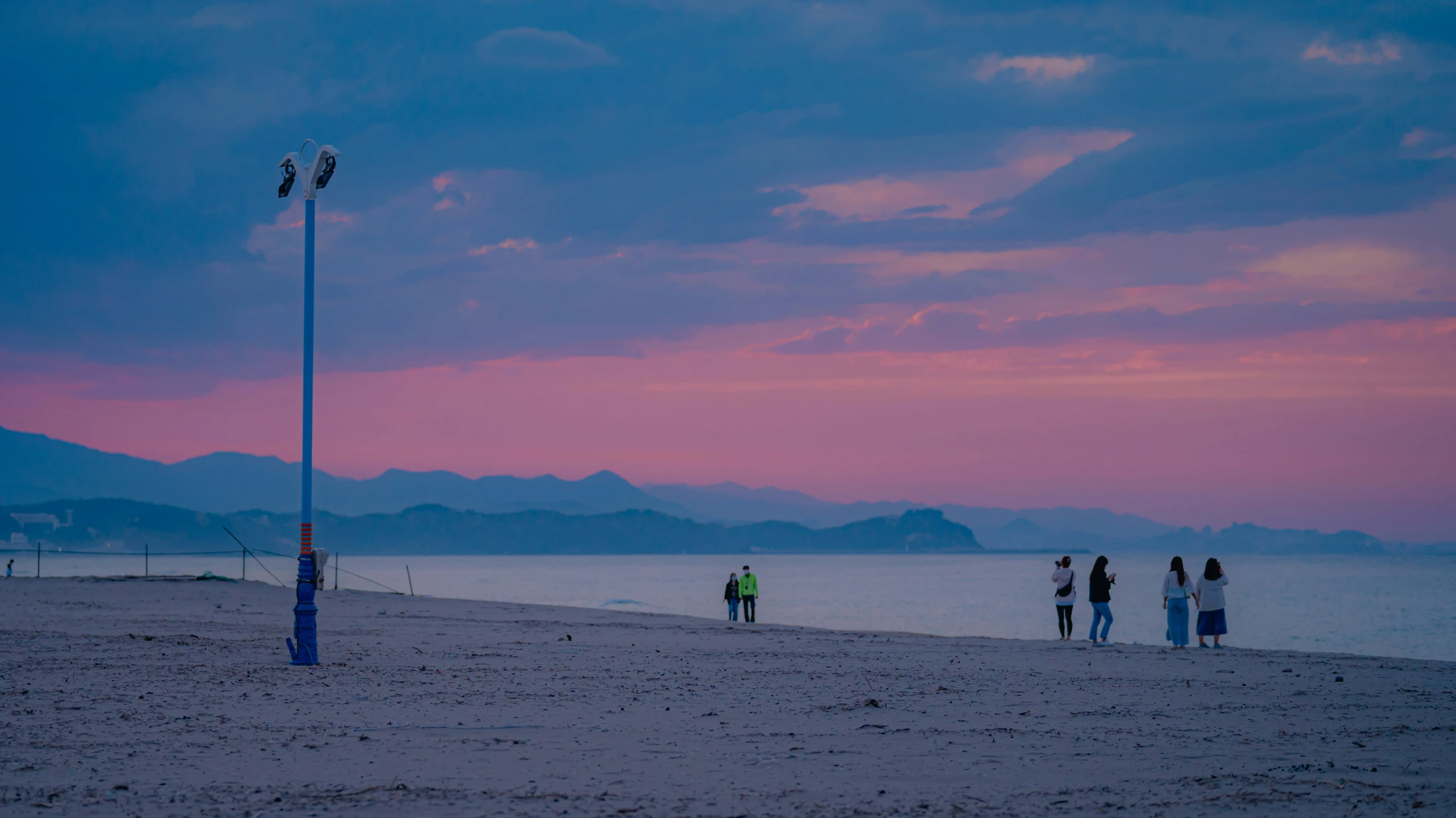 people are on the sand at sunset near the water