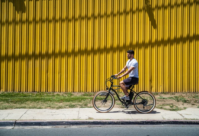 a man riding a bicycle past a yellow wall