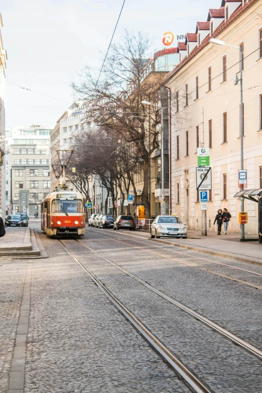 a trolley train on tracks near buildings and parked cars