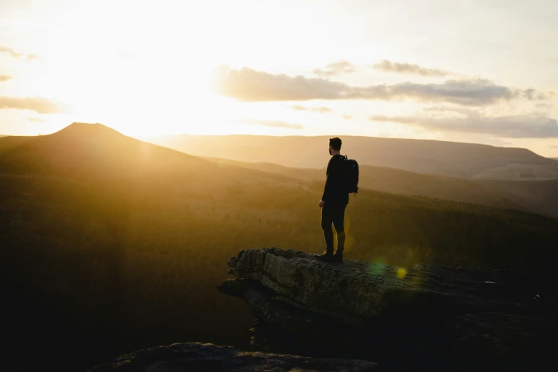 man on edge of cliff with setting sun