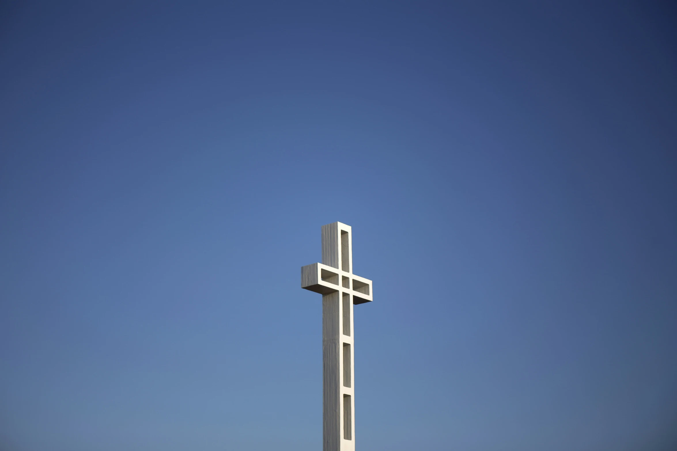 white cross statue on top of wooden structure against blue sky