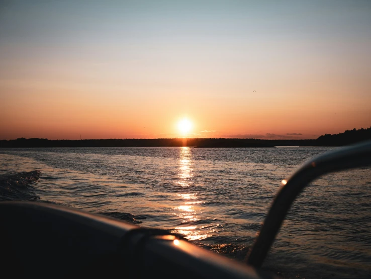 the sun sets behind a boat out on the water