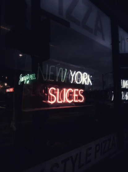 neon signs are lit up on the windows of a pizza shop