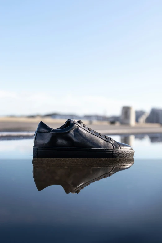 a black shoe is placed on a reflective surface with water in the background