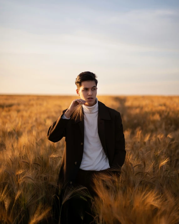 the boy is standing in a wheat field wearing a jacket