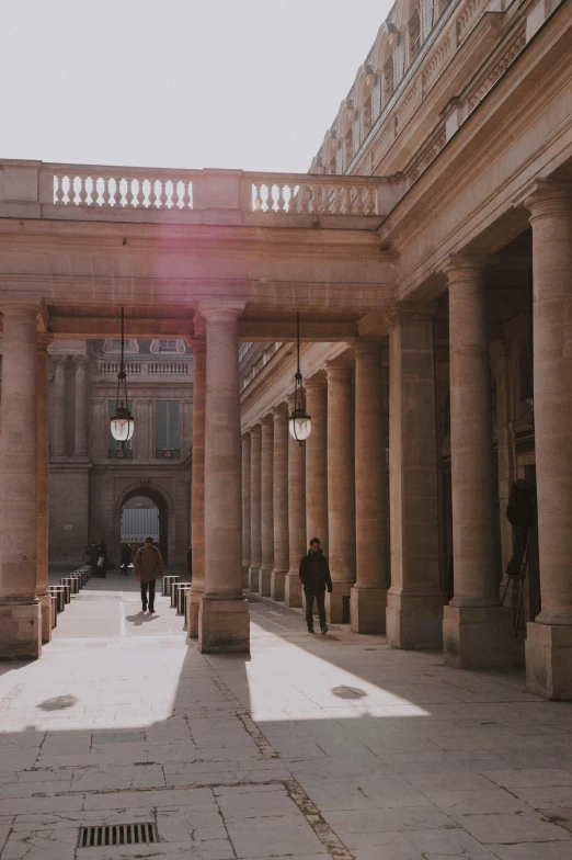 a group of people walking inside of a building with columns