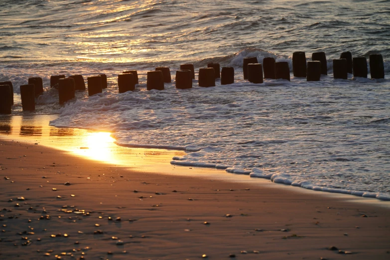 the sun is setting on the water with old posts