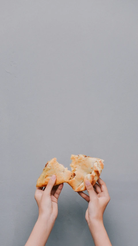 two hands hold up a piece of pizza