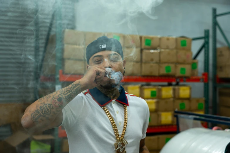 man in hat and white shirt with a chain around his neck smoking