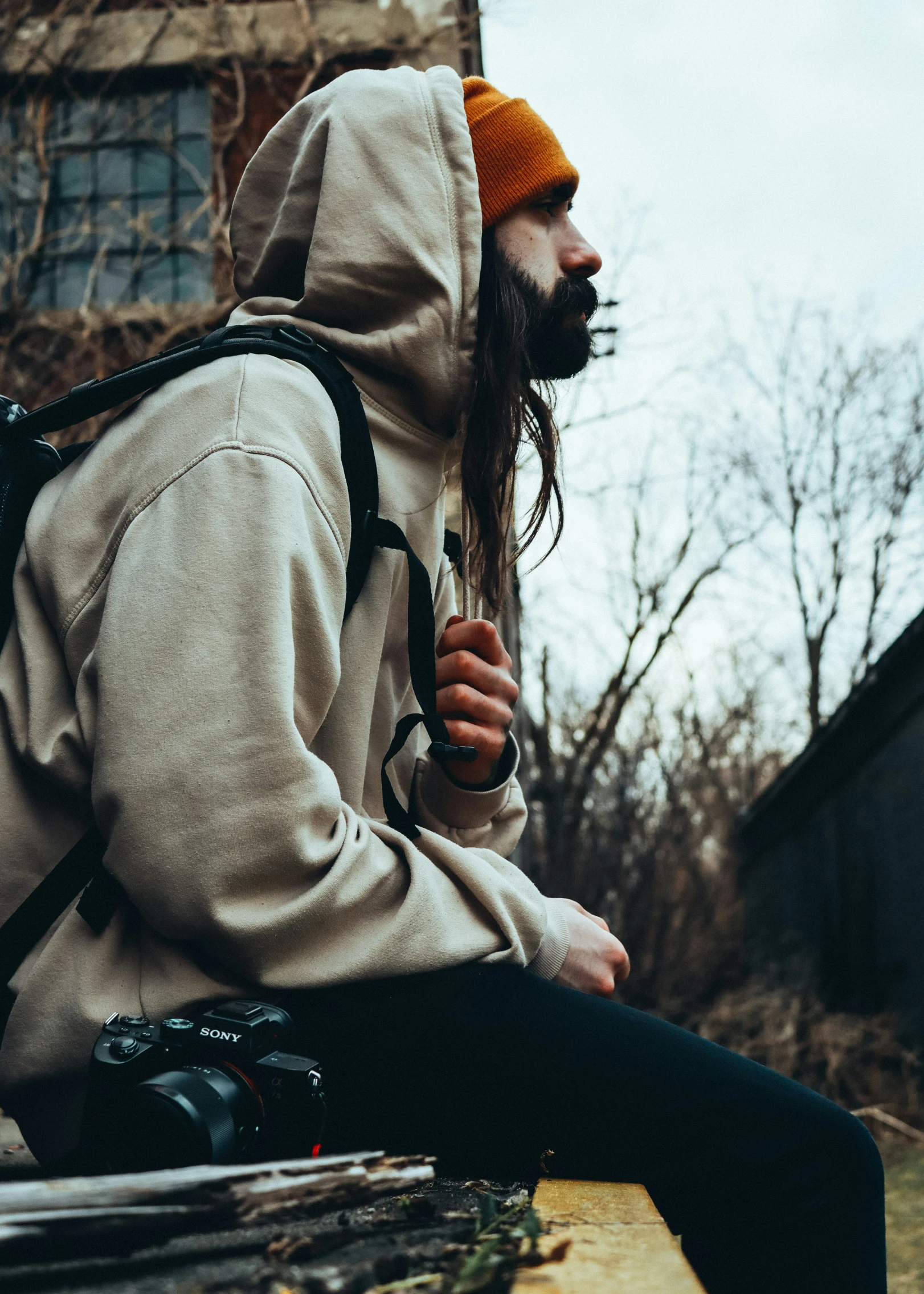 a man with long hair sitting on a bench wearing a backpack