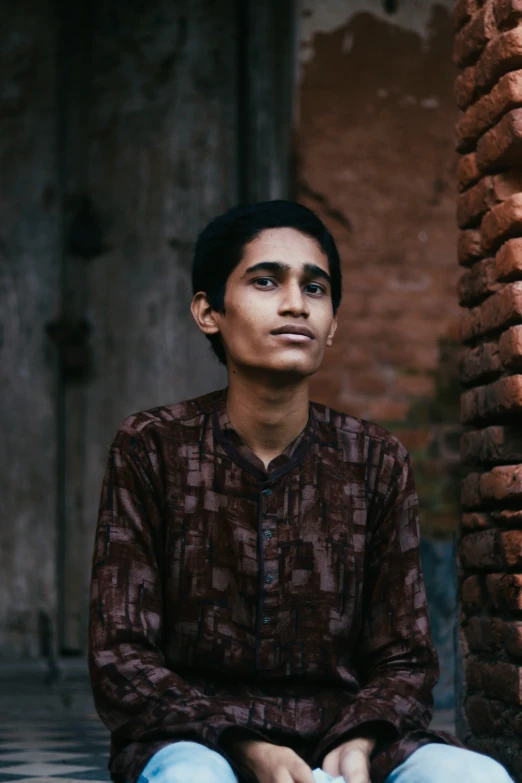 a boy sitting and staring in front of brick columns