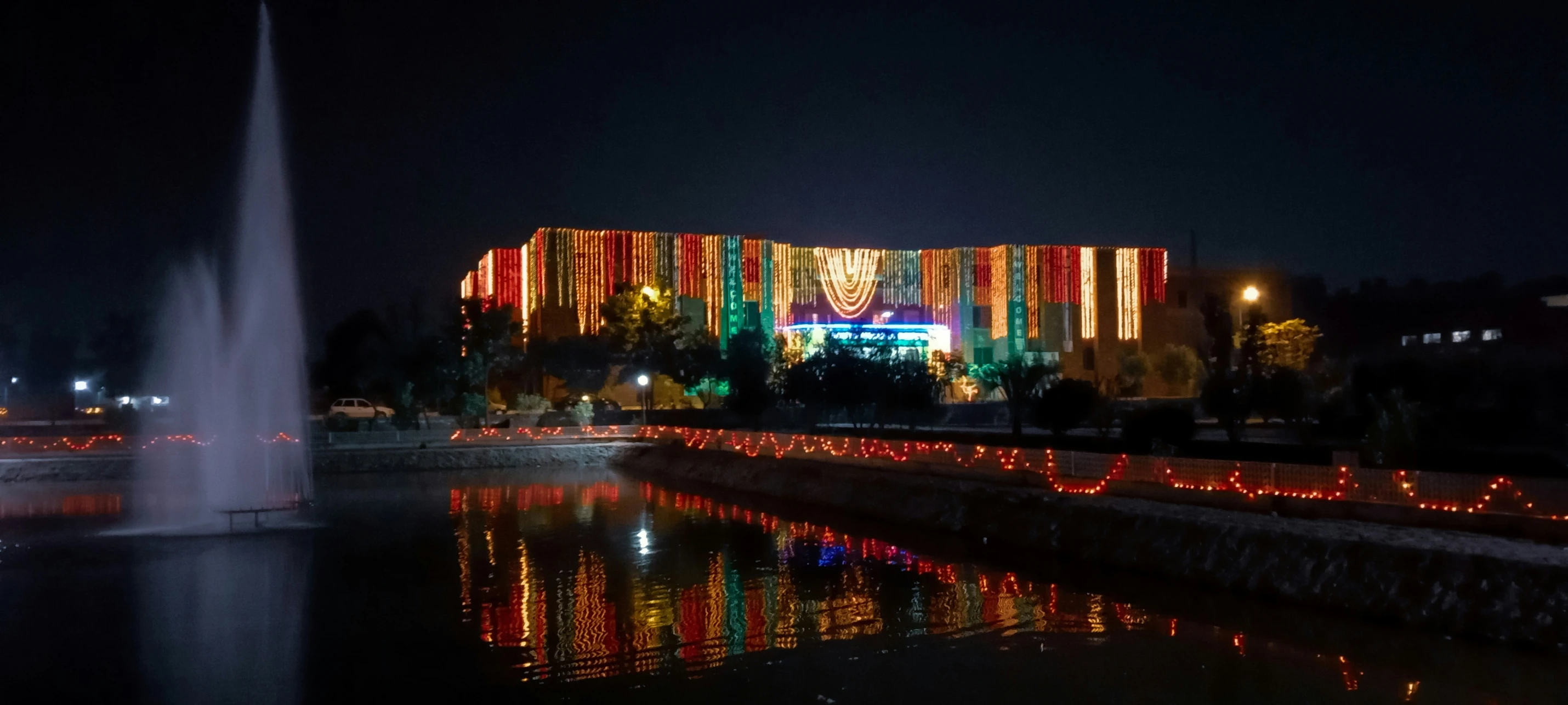 an illuminated building stands in the dark with water