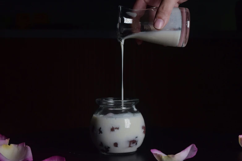 the hand is pouring milk in a jar