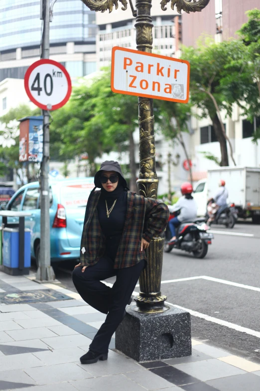 a woman in black jacket and hood standing under a sign on a pole