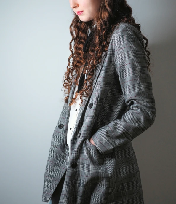 woman wearing a checked blazer standing up against a gray background