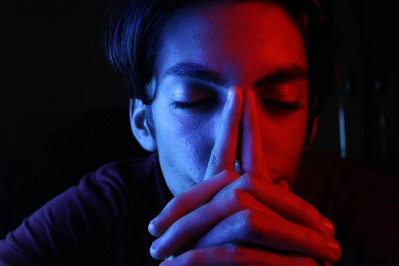 a man in a dark room holding his face next to his hand