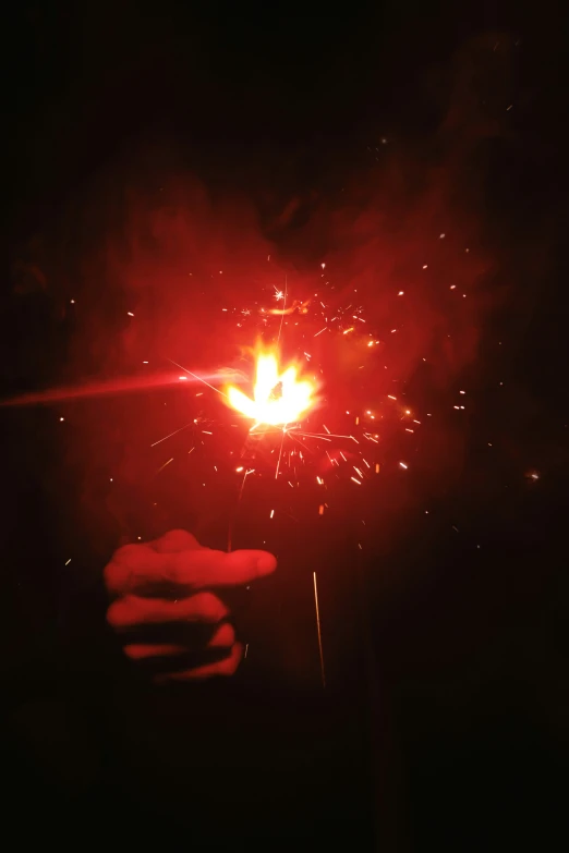 a hand holding a lit fireworks in the dark
