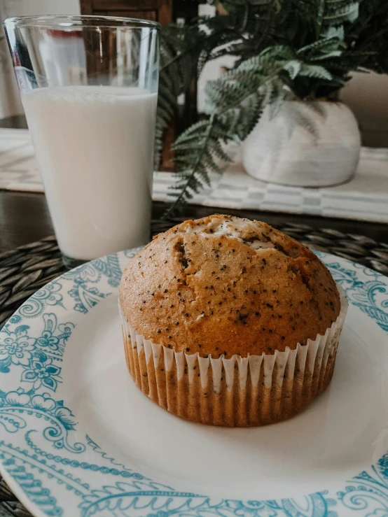 a muffin sits on a plate beside a glass of milk