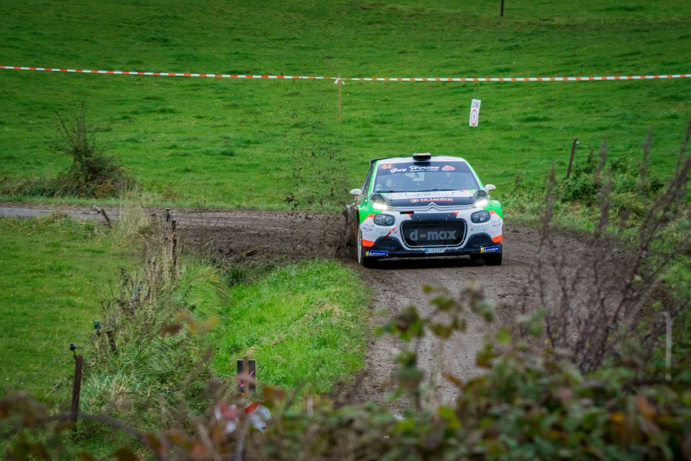 a rally car driving down a muddy track