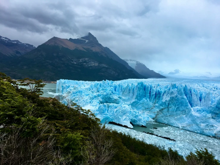 a large blue iceberg sitting below some mountains