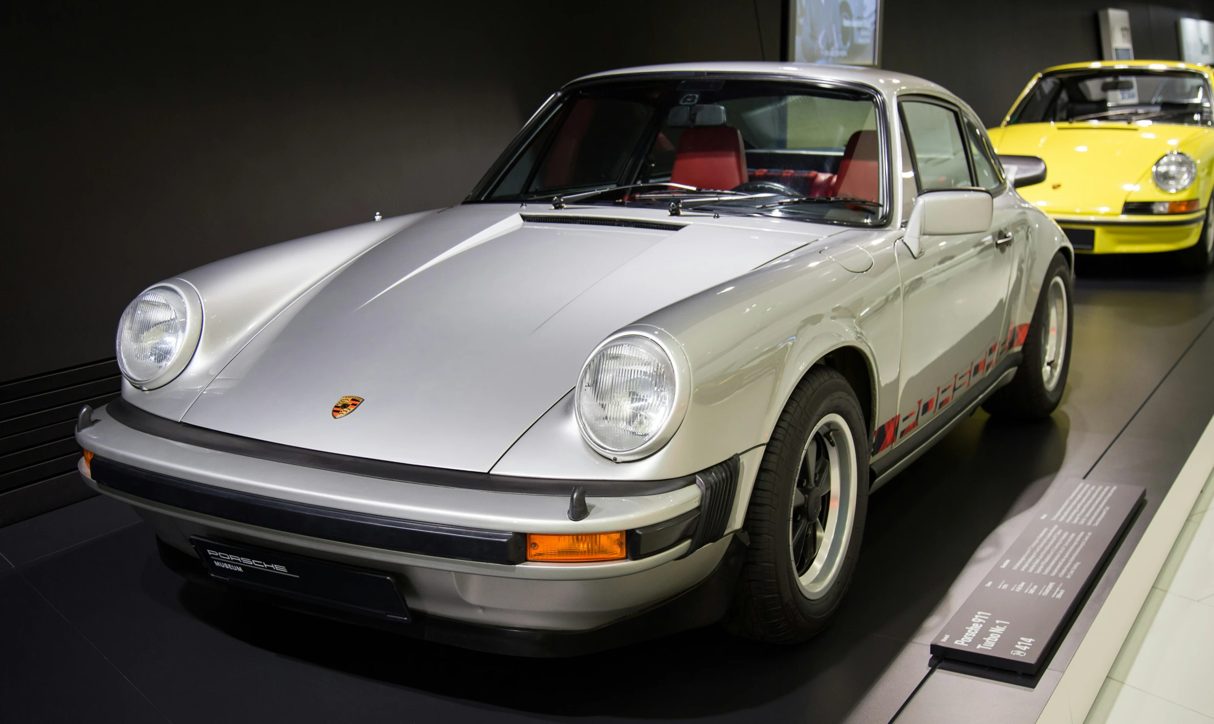 a silver and yellow porsche coupe parked on display