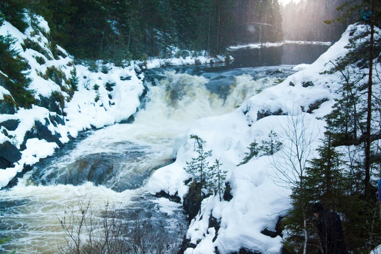 a person walking in the snow next to a rushing river