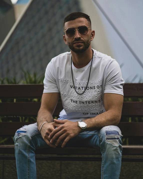 a young man is sitting on a bench wearing sunglasses