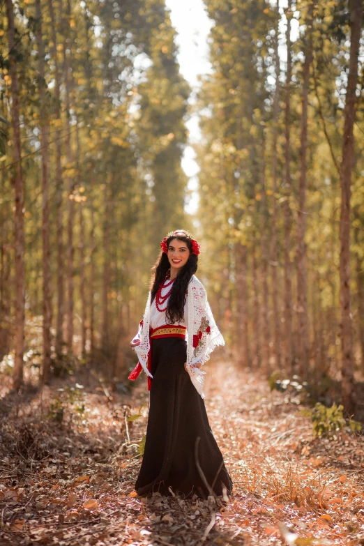 a young woman dressed in traditional mexican clothing poses on a leaf covered trail