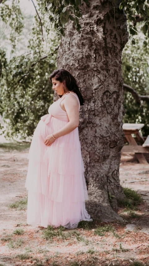 a pregnant woman standing by a tree in a dress