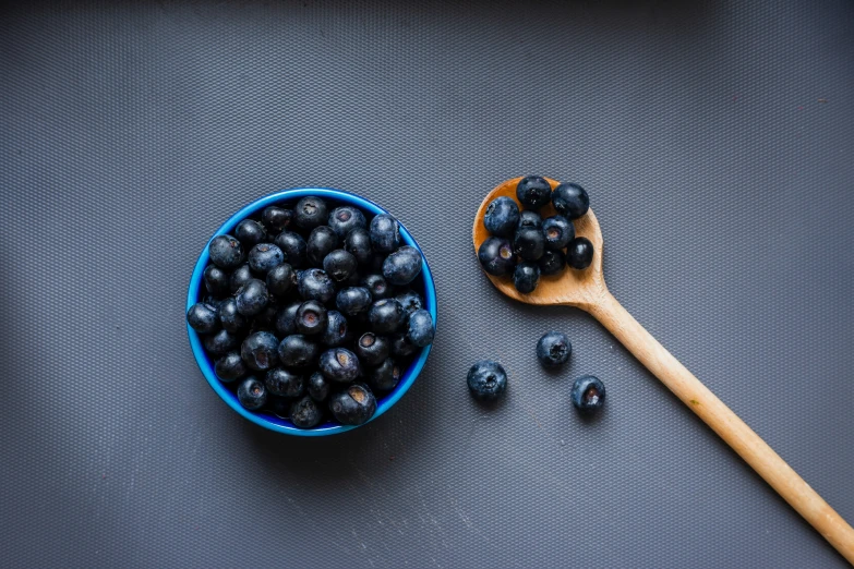 a wooden spoon on a gray surface next to blue berries