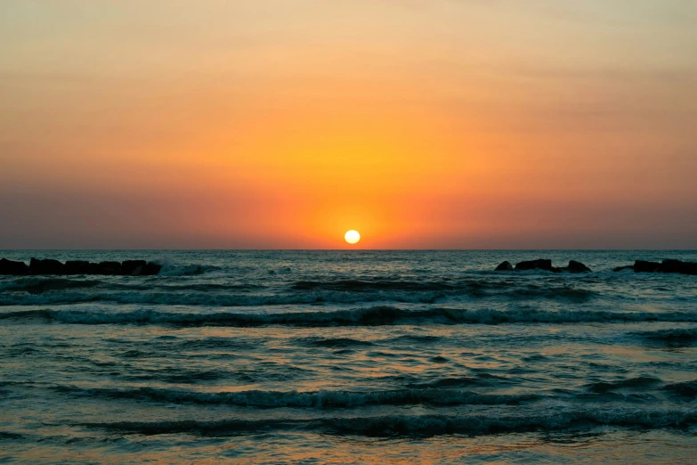 the sun setting over the ocean in front of the waves