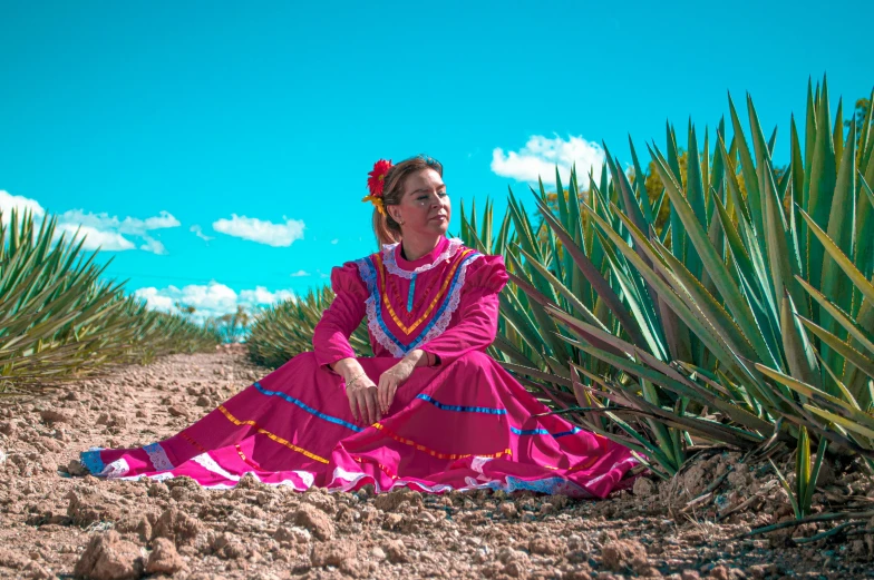 a girl in an old mexican dress sits in a desert with tall grass