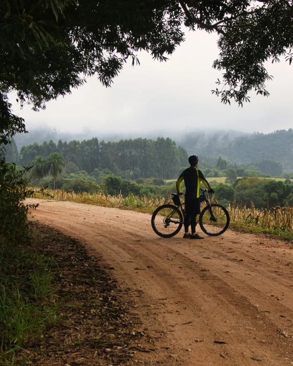 a man with a bicycle on the side of a dirt road