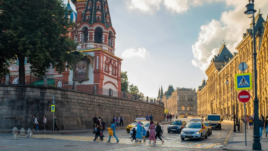 people walk along a cobblestone street past two old building