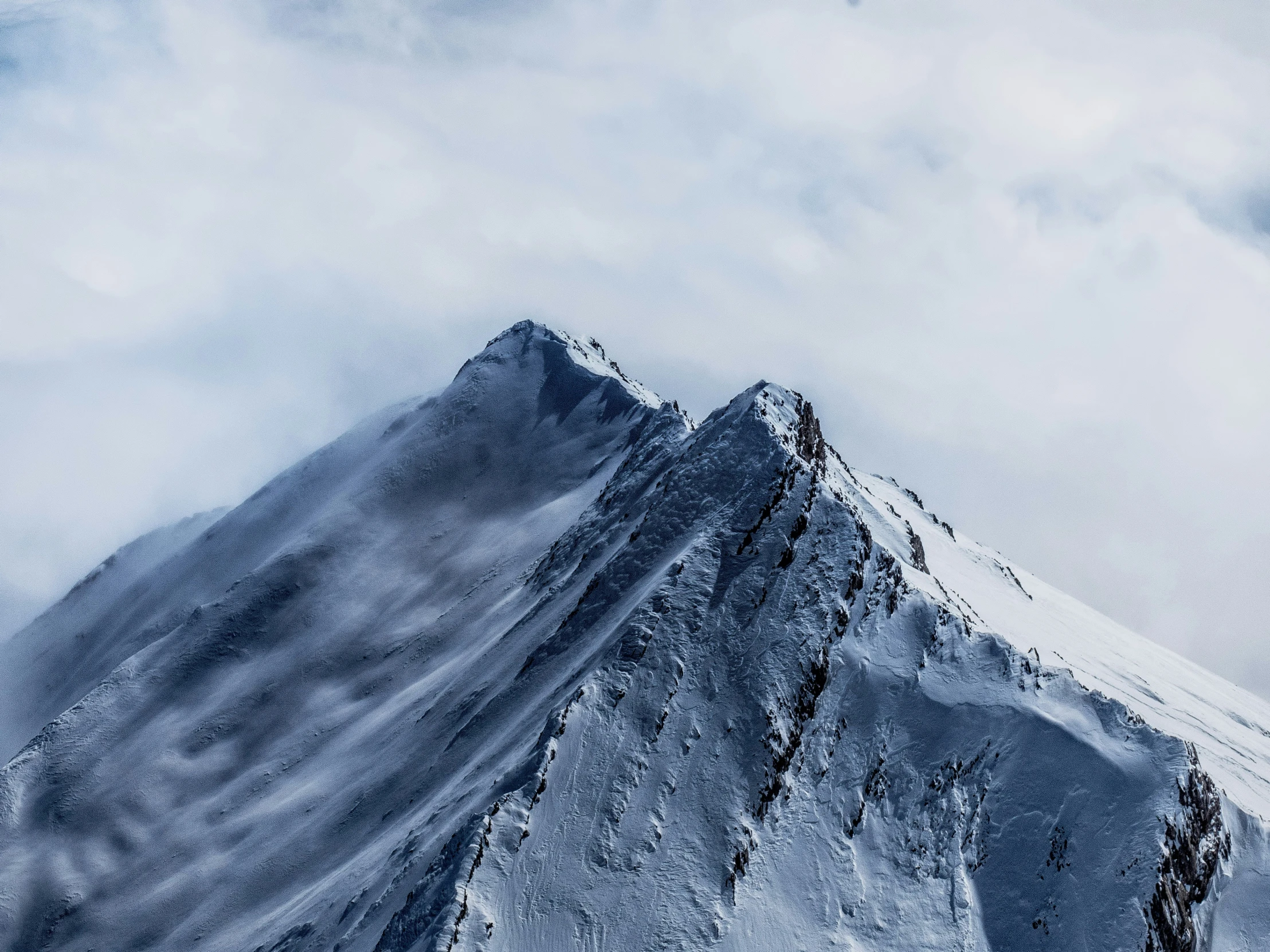 a snow covered mountain is pictured against a cloudy sky