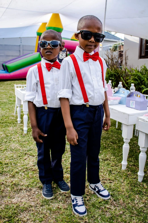 two boys are wearing sunglasses standing near a table