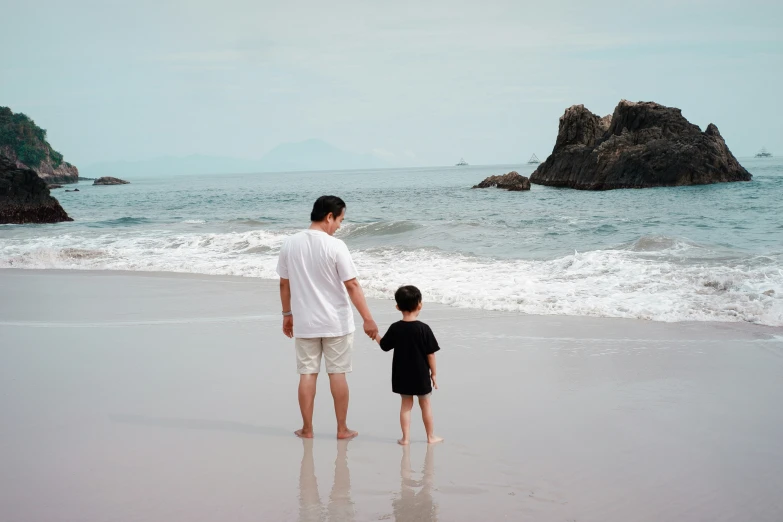 a man and a boy stand on the beach next to some waves