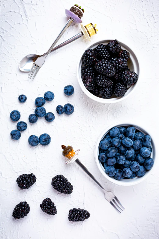 several bowl of berries and blueberries, one with a fork next to a spoon