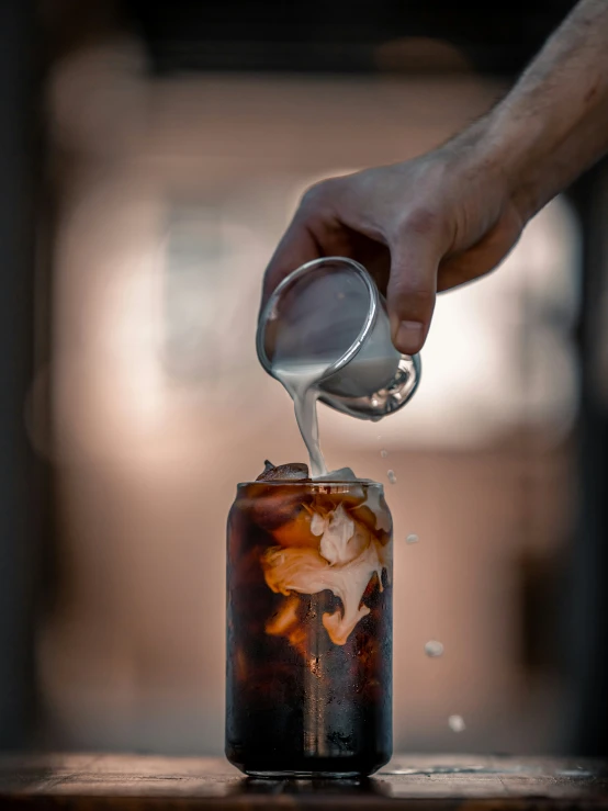 person pouring a beverage into a can with ice and soda