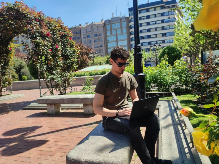 a man is sitting on a bench working on his laptop