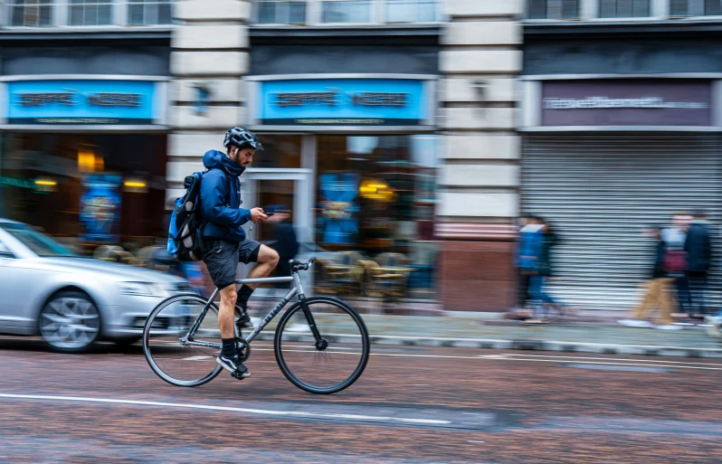 a bicyclist rides along the street in front of some stores