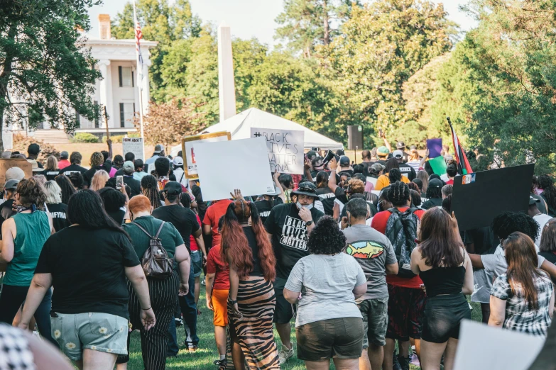 many people gathered around in a field with a sign