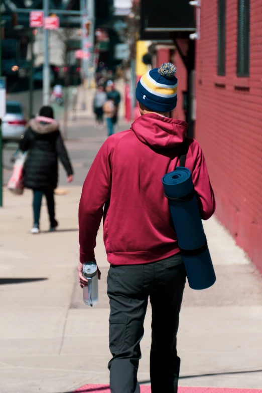 the back of a man carrying a water bottle walking down the sidewalk