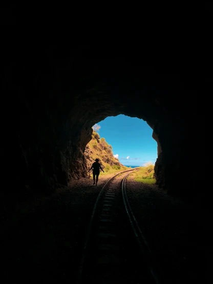 silhouette of a man walking on train tracks into a tunnel