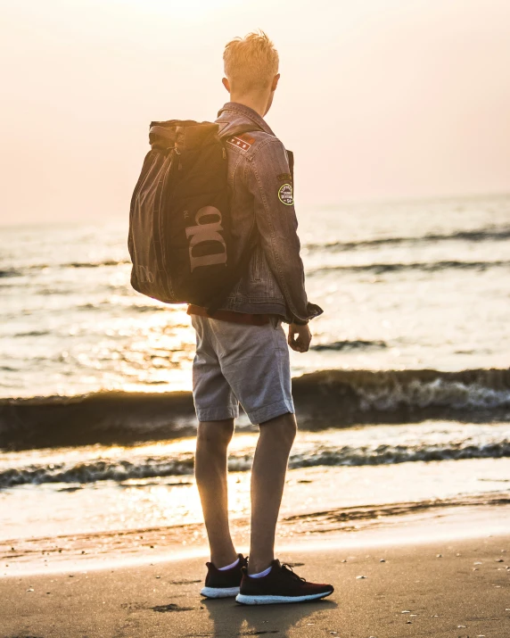 a man at the beach looking at the water with his backpack