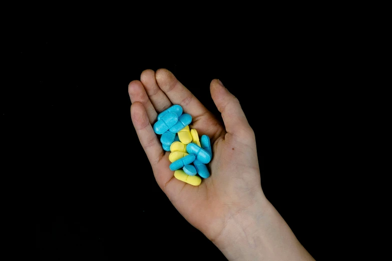 a hand holding some colorful pills next to a black background