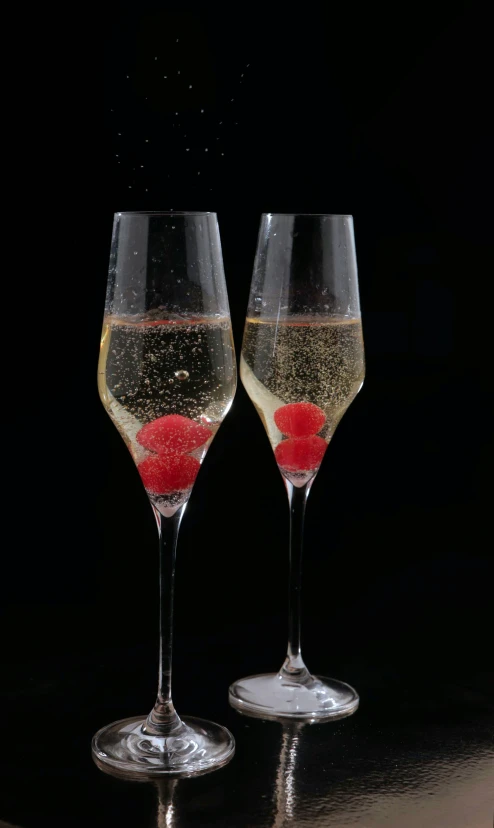 two champagne glasses with a red fruit floating in the water