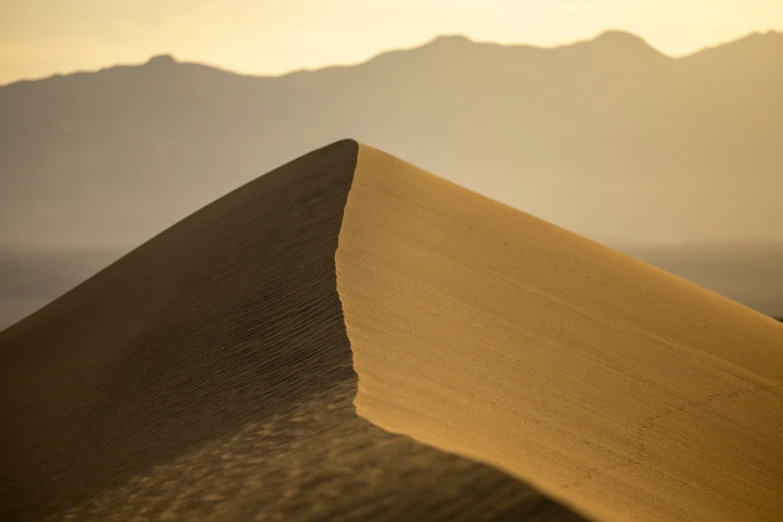 a very tall dune on a desert with a mountain in the distance