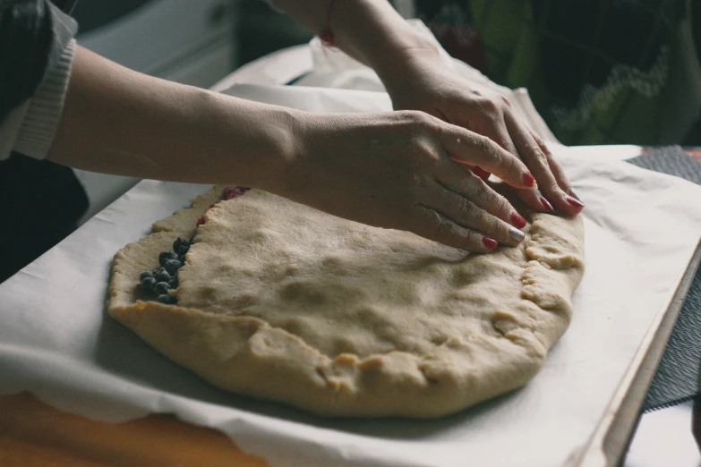 woman's hand over top of an uncooked pie crust on white paper