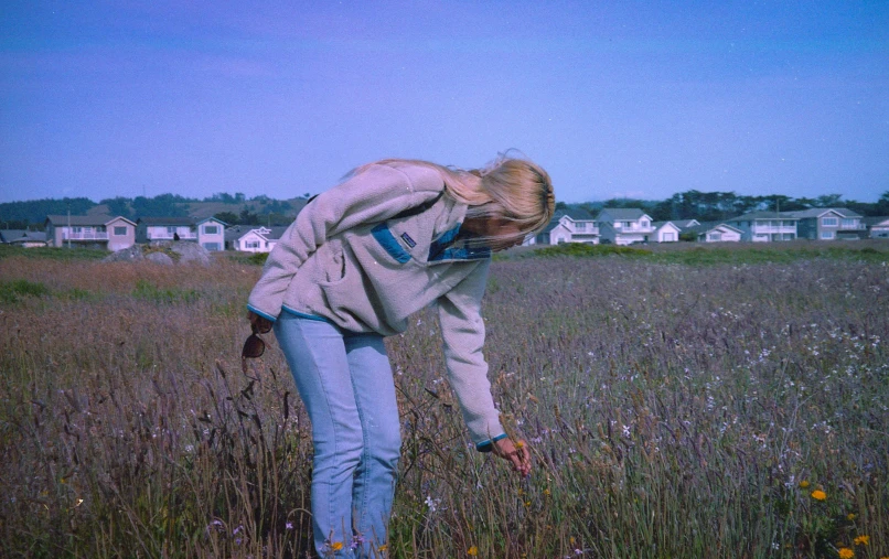 a woman in jeans stands in the middle of a field with wildflowers